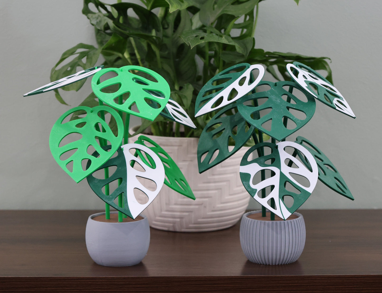 Decorative artificial plants with green and white leaves in small pots on a wooden surface.