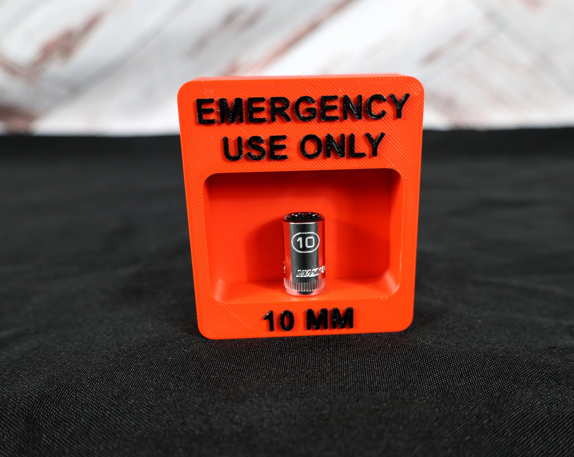 Red container labeled 'Emergency Use Only' with a 10mm object inside on a black background