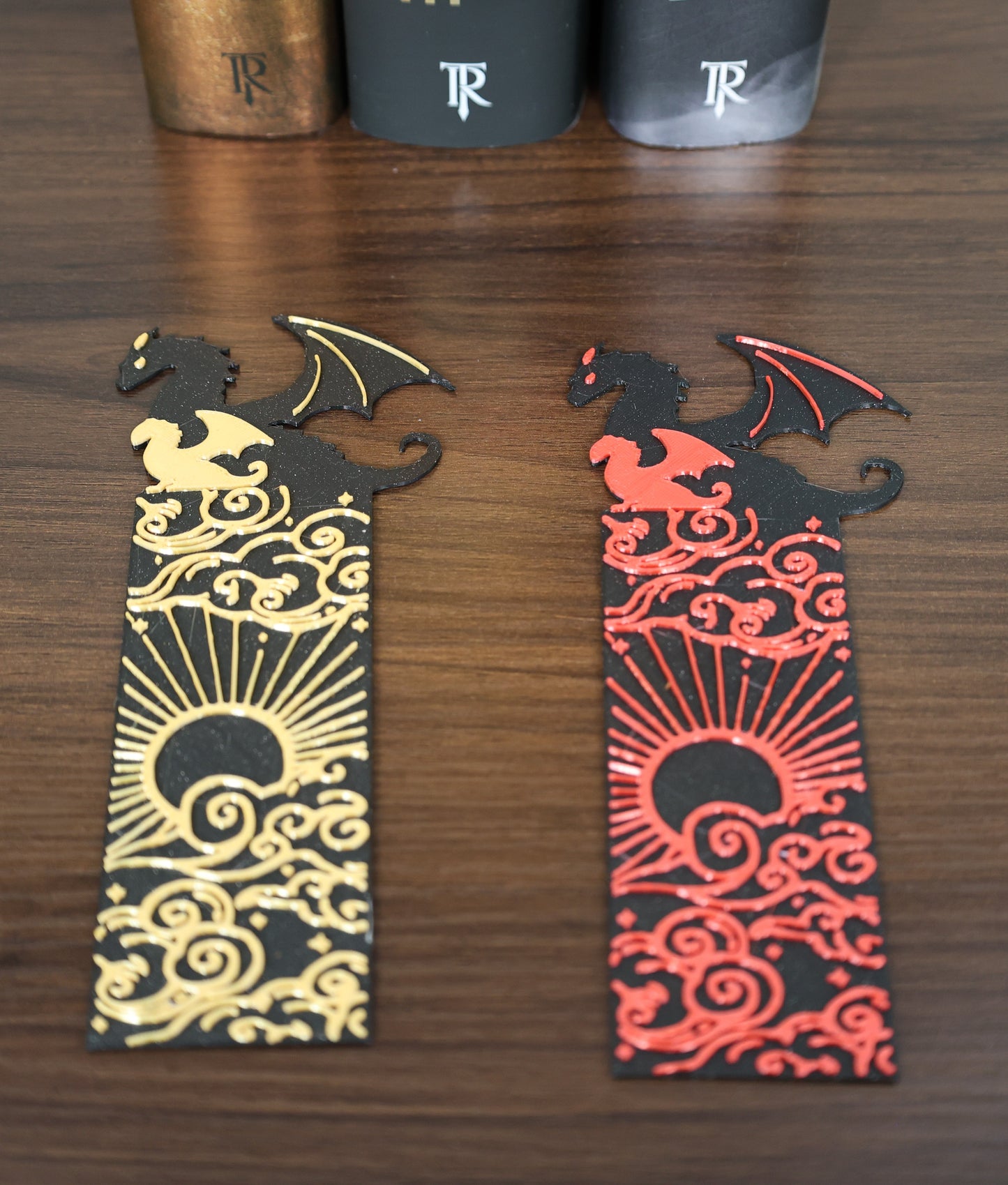 Two dragon-themed bookmarks, one gold and one red, on a wooden surface.