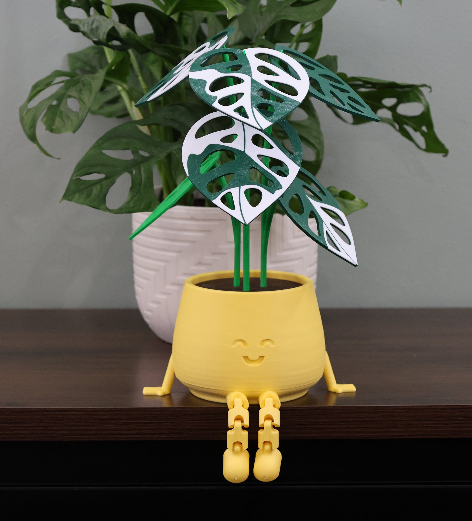 Yellow plant pot with cartoon face and leaf design on a wooden surface